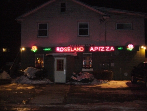 The neon-lit exterior of Roseland Apizza, covered with January snow.